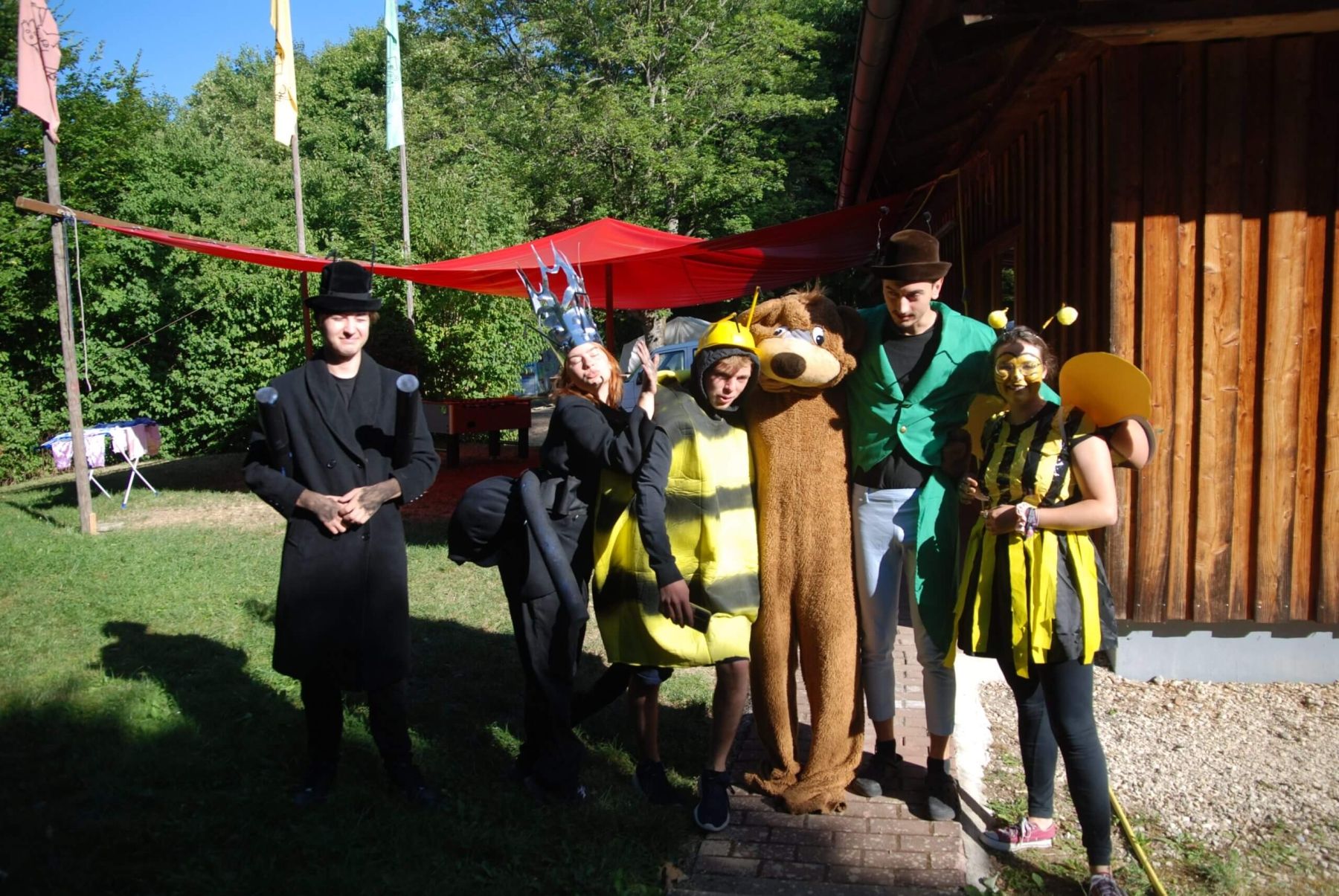 Mehrere Betreuerinnen und Betreuer in fantasievollen Kostümen posieren lachend vor einer Holzhütte.