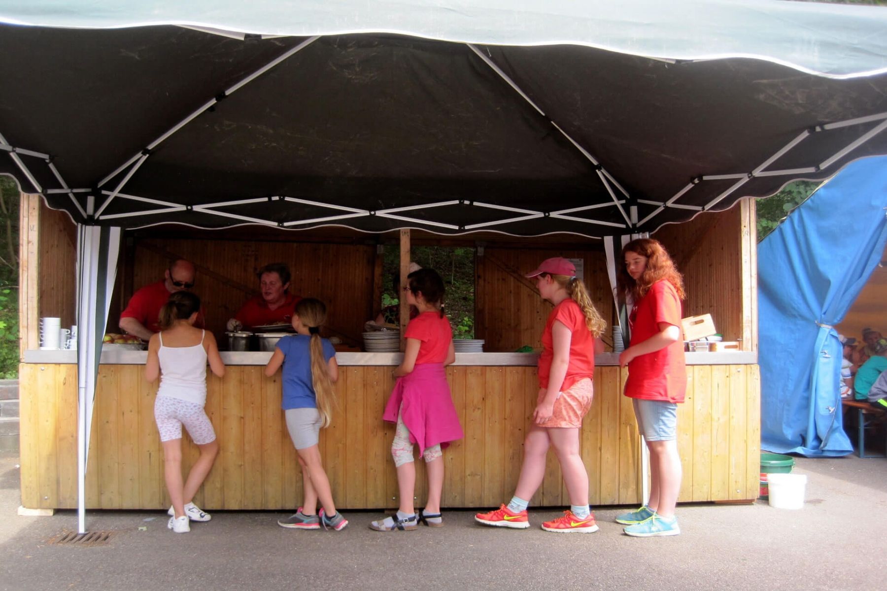 Kinder und Jugendliche stehen an einem Essensstand unter einem Pavillon.